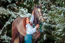 Девушка в белом свитере и в синих джинсах стоит с конём в заснеженном лесу на фоне елей, работа исполнена Под масло, художник Юлия 